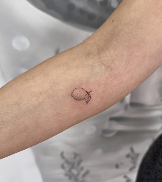 Micro tatuaje minimalista de limón en línea fina, brazo — Madrid